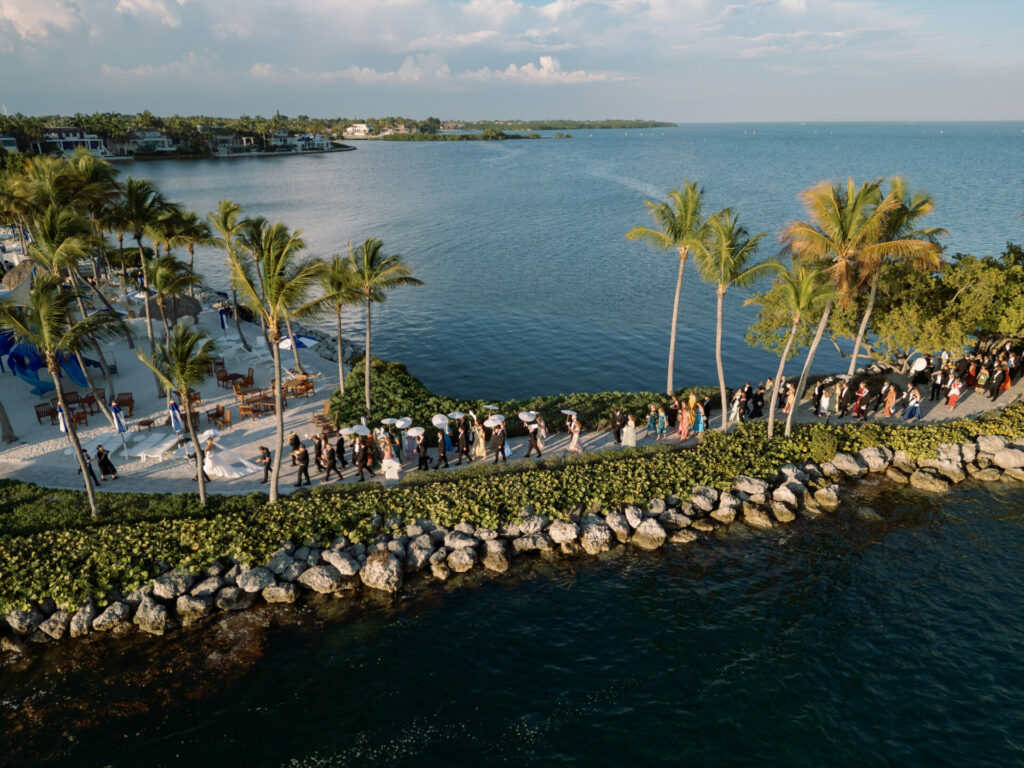 People walk along palm-lined path by ocean.