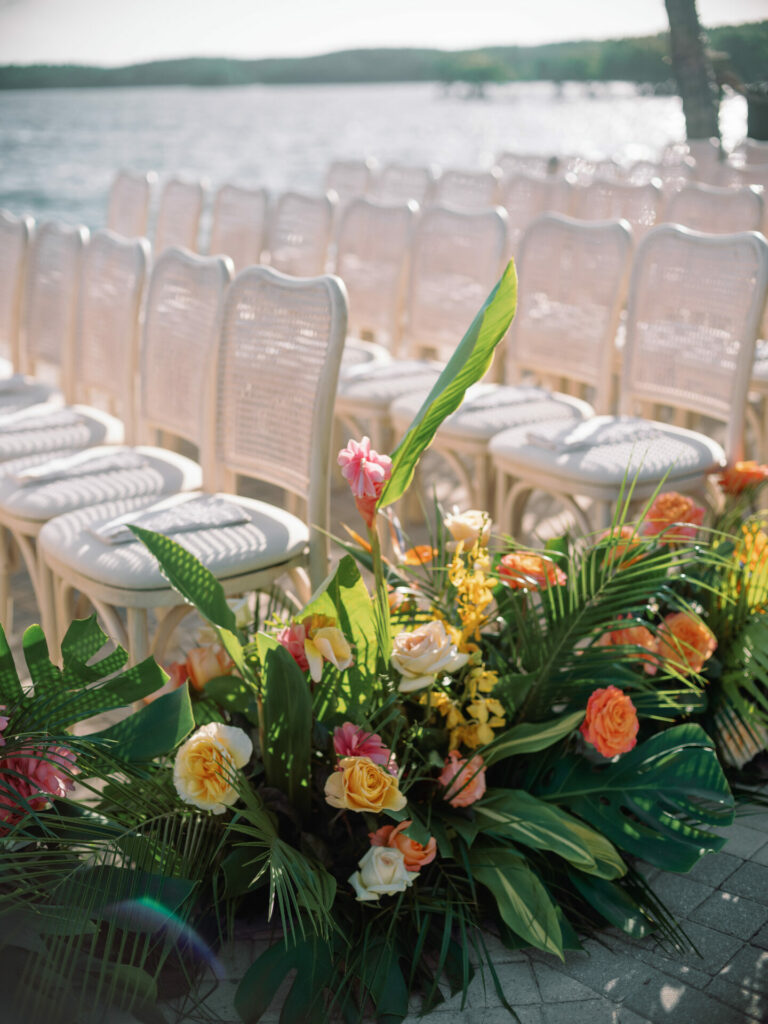 White chairs and flowers by sunlit waterfront ceremony.