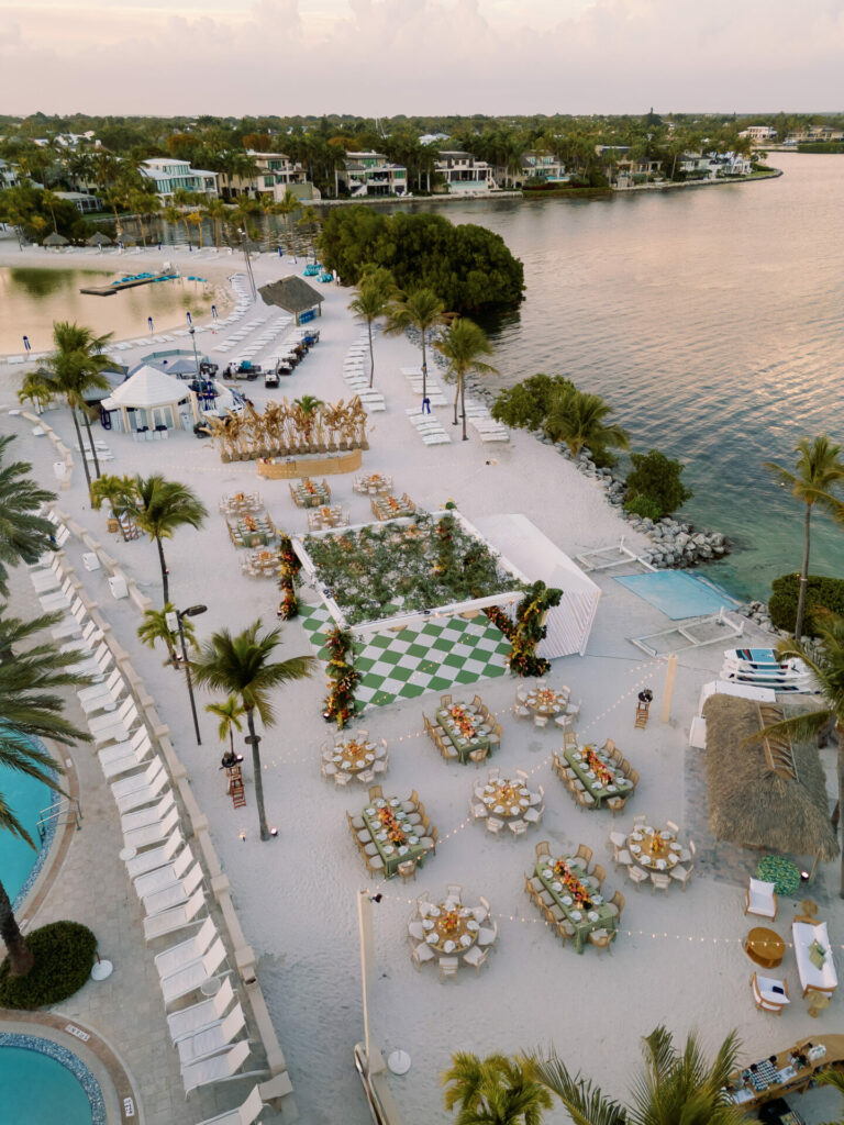 Beachside event at sunset with tables, checkered floor, palm trees.