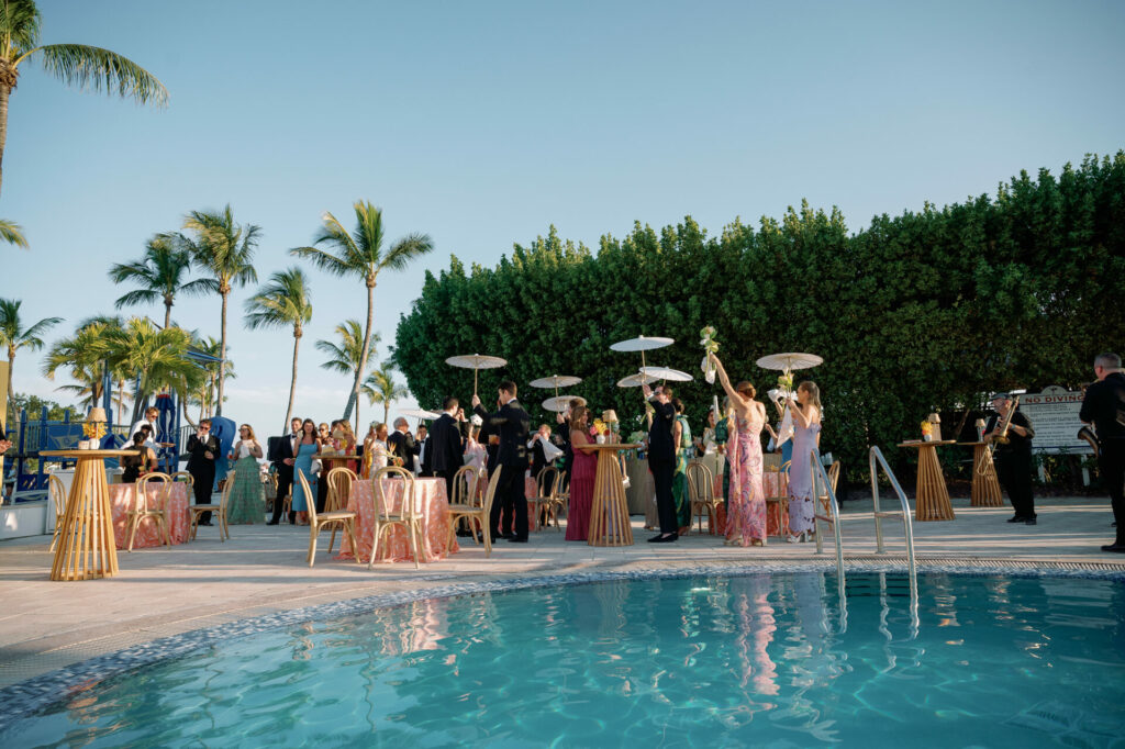 Formally dressed guests gather poolside at luxury outdoor wedding.