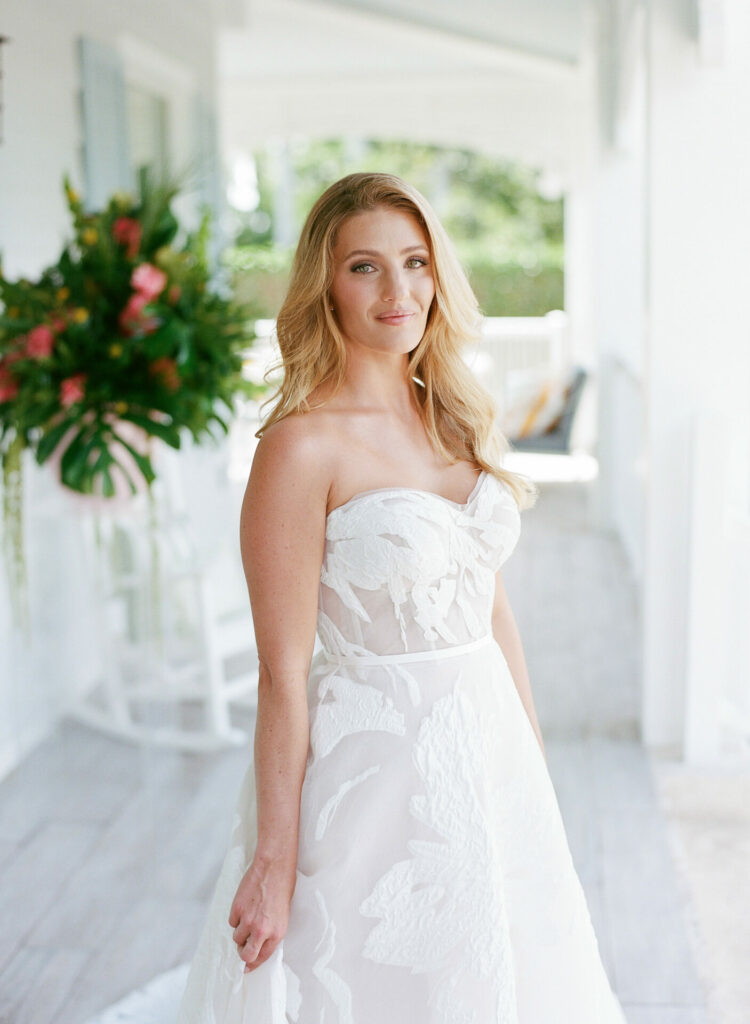 Blonde woman in floral white wedding dress on porch.