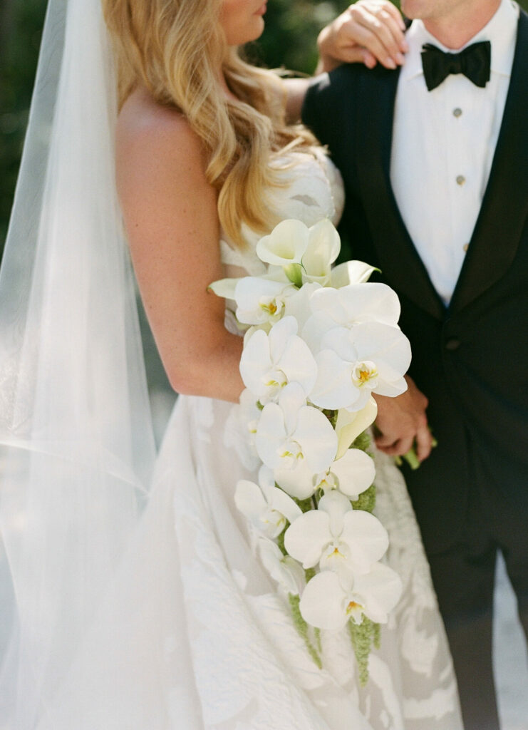 Bride in couture with orchid bouquet beside groom.