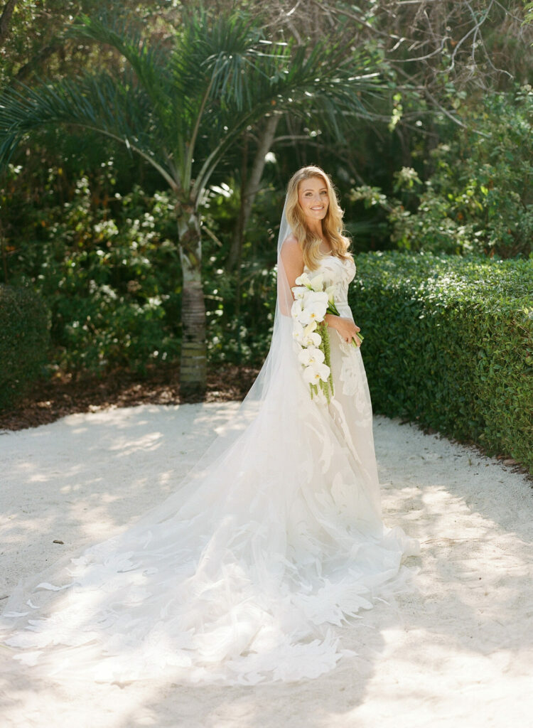 Bride in luxury white gown with bouquet outdoors.