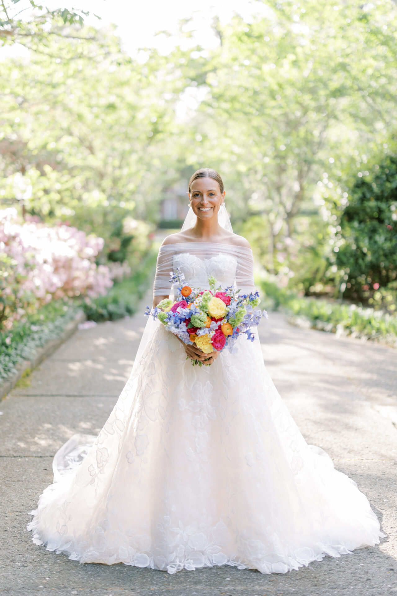 Bride in white gown smiling with bouquet outdoors.