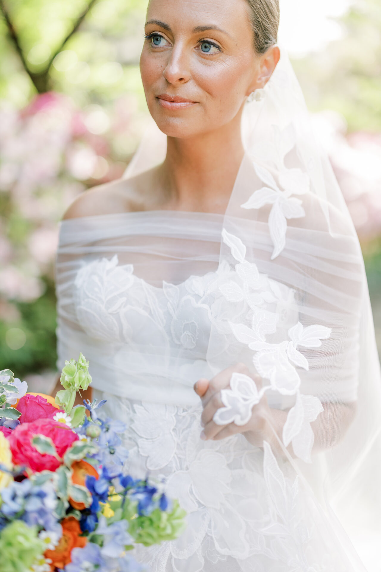 Bride in lace dress holds bouquet outdoors, sunlight.