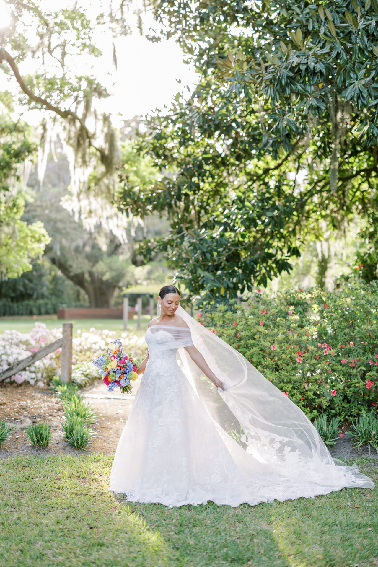 Bride in lace gown with bouquet, sunlit garden.