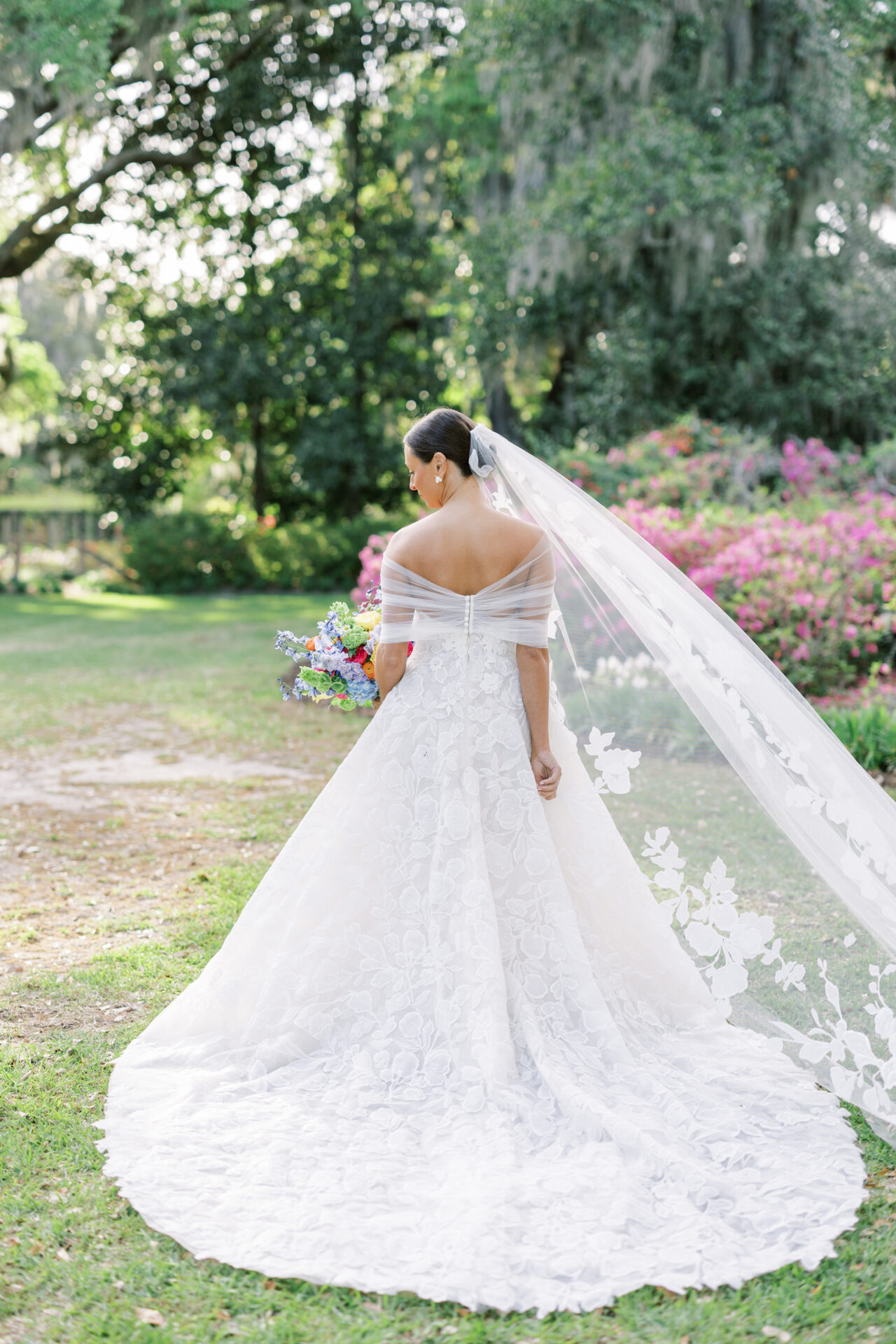 Bride in white gown and floral veil outdoors, bouquet.