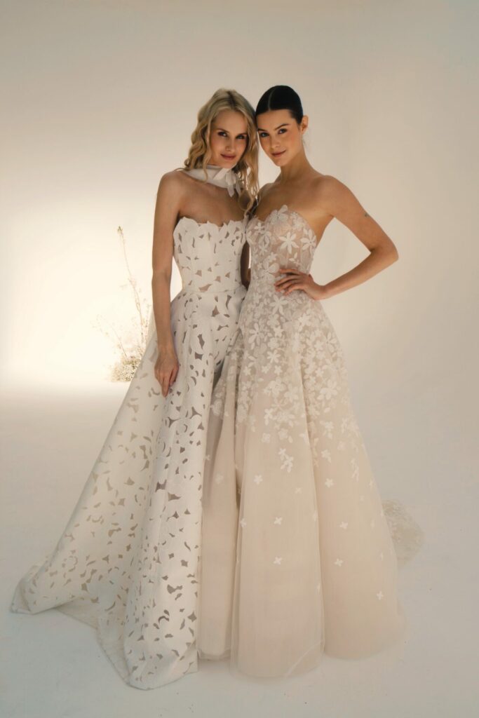 Two women in floral white gowns pose together.