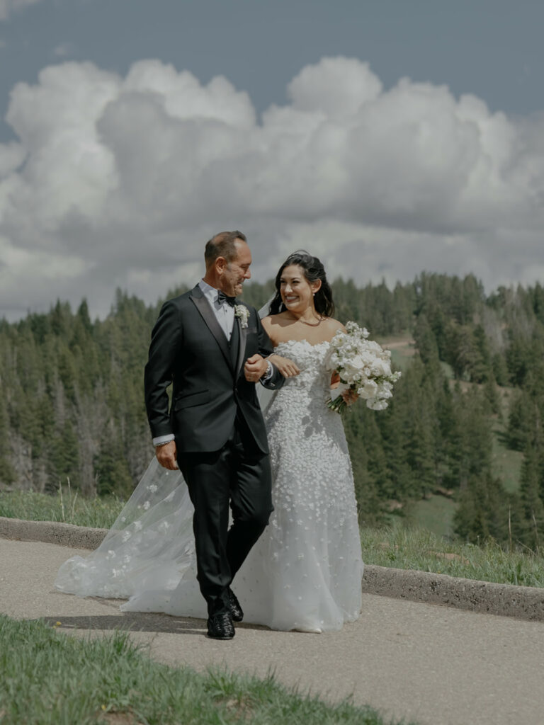Bride and groom walking arm-in-arm, smiling outdoors.