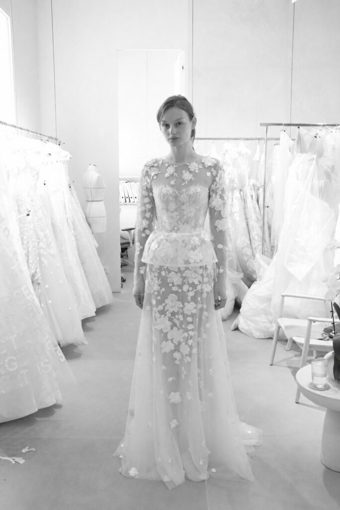 Woman in floral bridal gown among dresses in boutique.