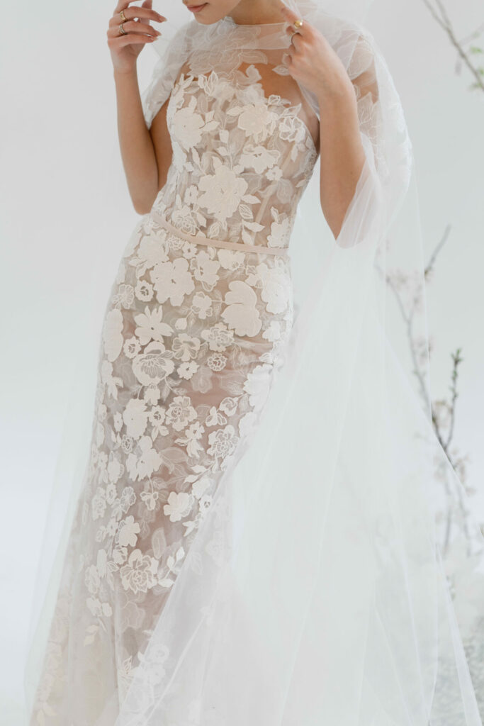 Woman in sheer white lace wedding dress, face hidden.