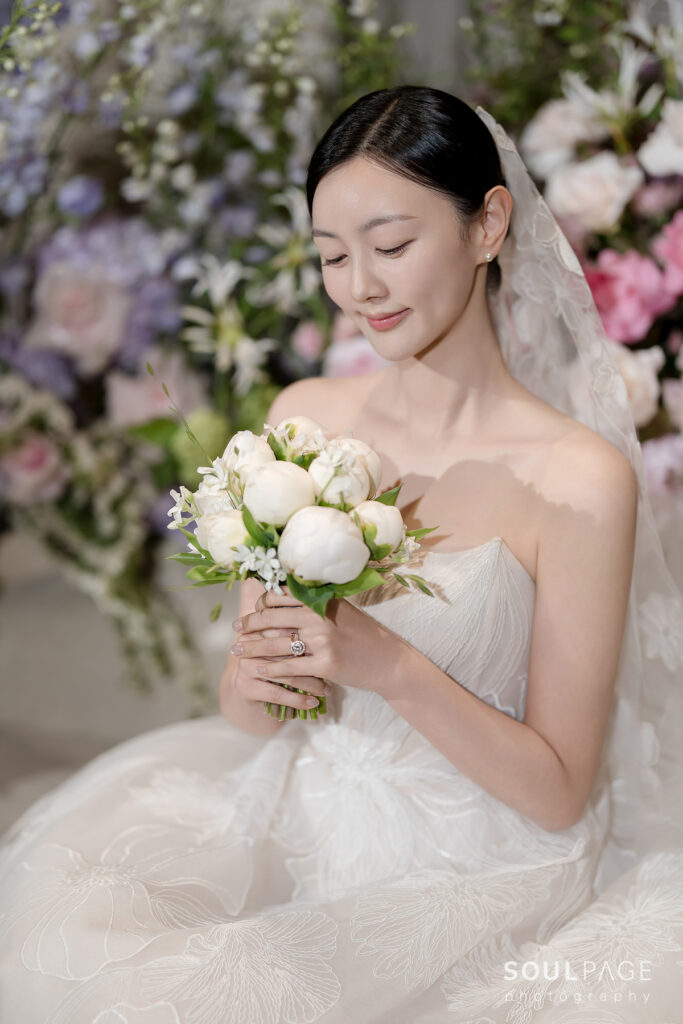 Bride in white gown, eyes closed, holding flowers.