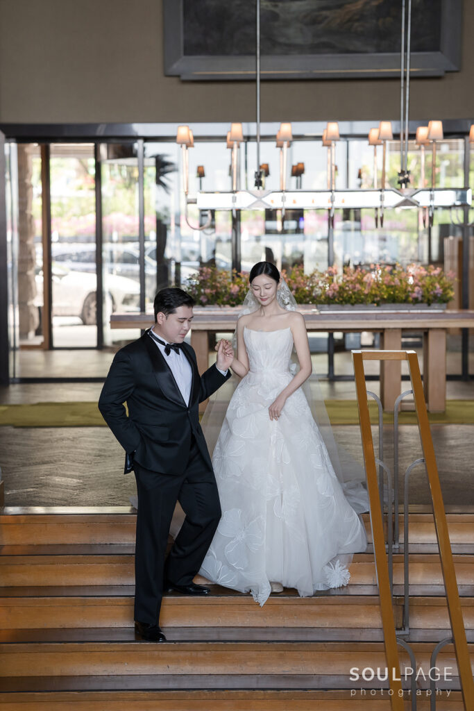 Bride and groom descend wooden steps in bright venue.