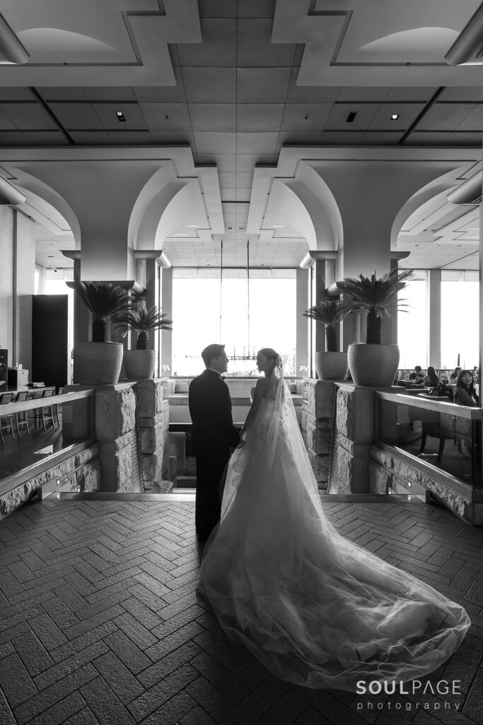 Bride and groom hold hands under grand arches, backlit.