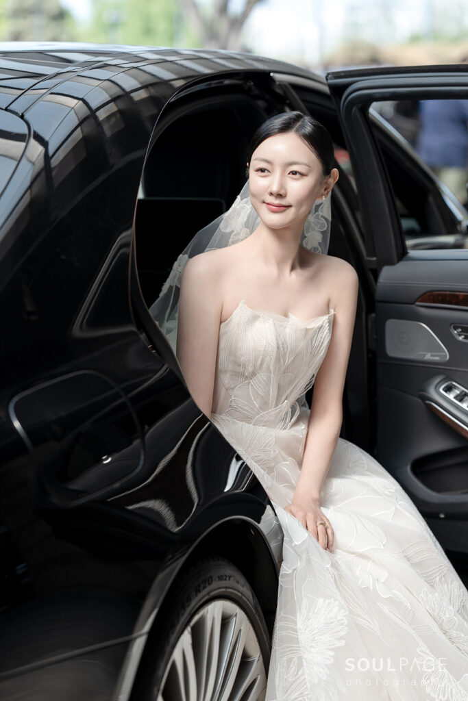 Bride in white dress smiles in car doorway.