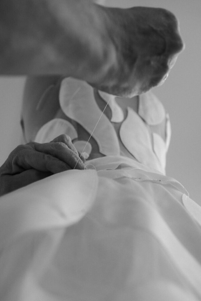 Hands sewing leaf appliqués onto fabric, black and white.