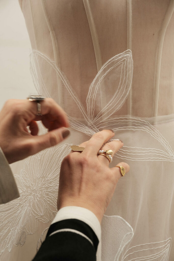 Ringed hands sew sheer, embroidered floral dress.