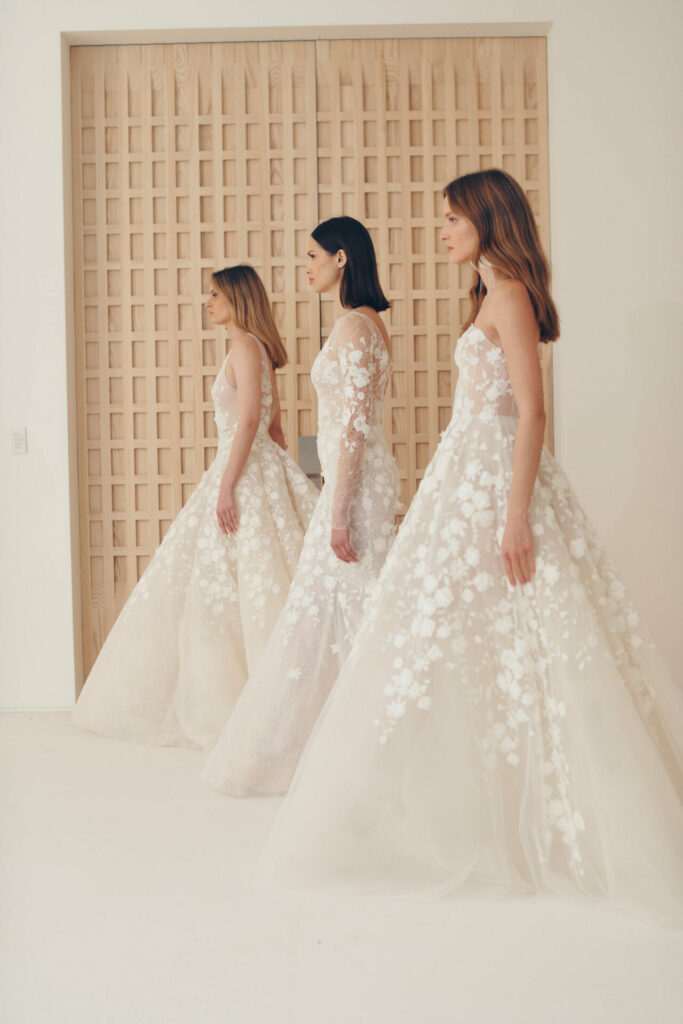 Three women in floral white gowns stand together indoors.
