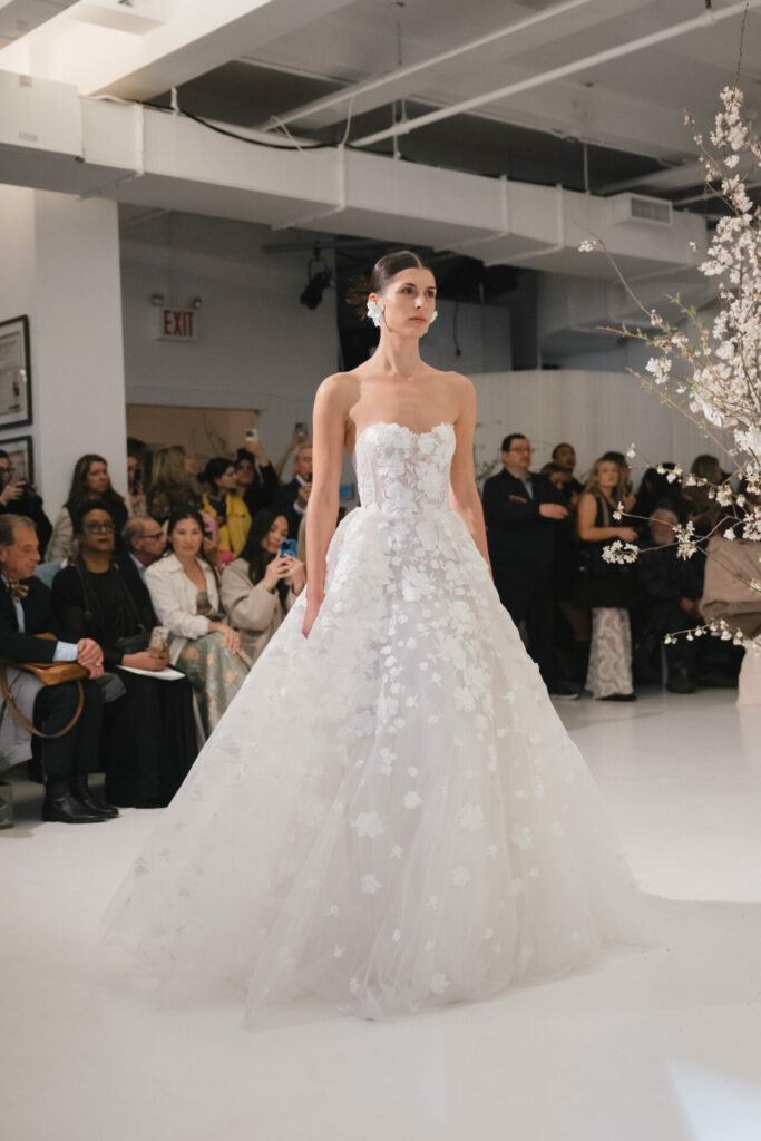 Model in white floral ballgown walks runway.