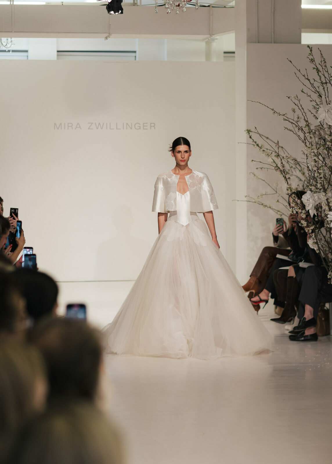 Model in white Clea dress walks runway; audience watches.