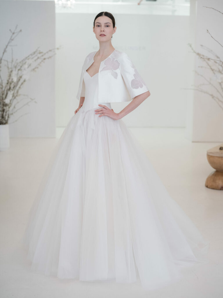 Bride in white gown and capelet, minimalist room.