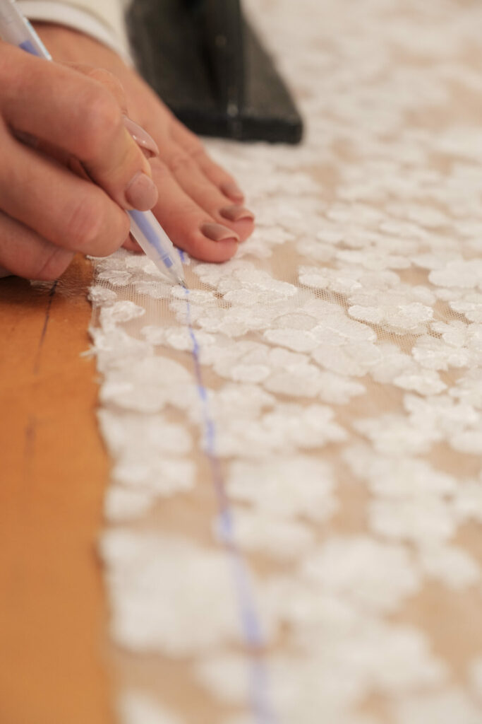 Hand marks blue line on white lace fabric.