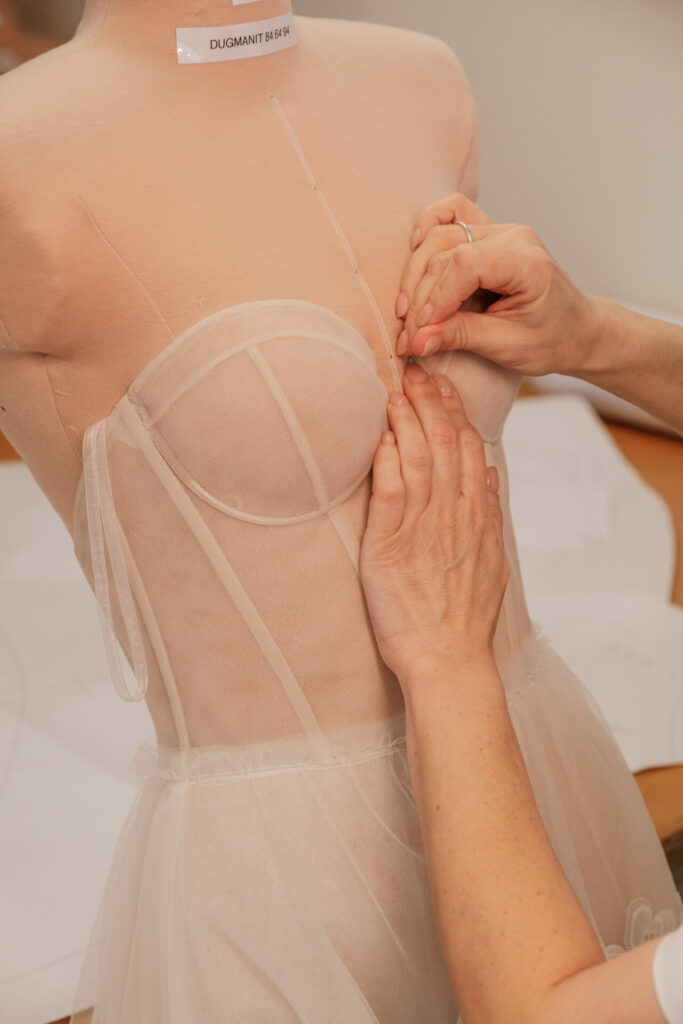 Hands pinning sheer fabric onto dress form bust.