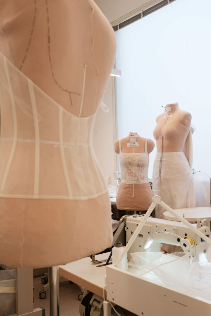 Three dress forms with white garments, sewing machine nearby.