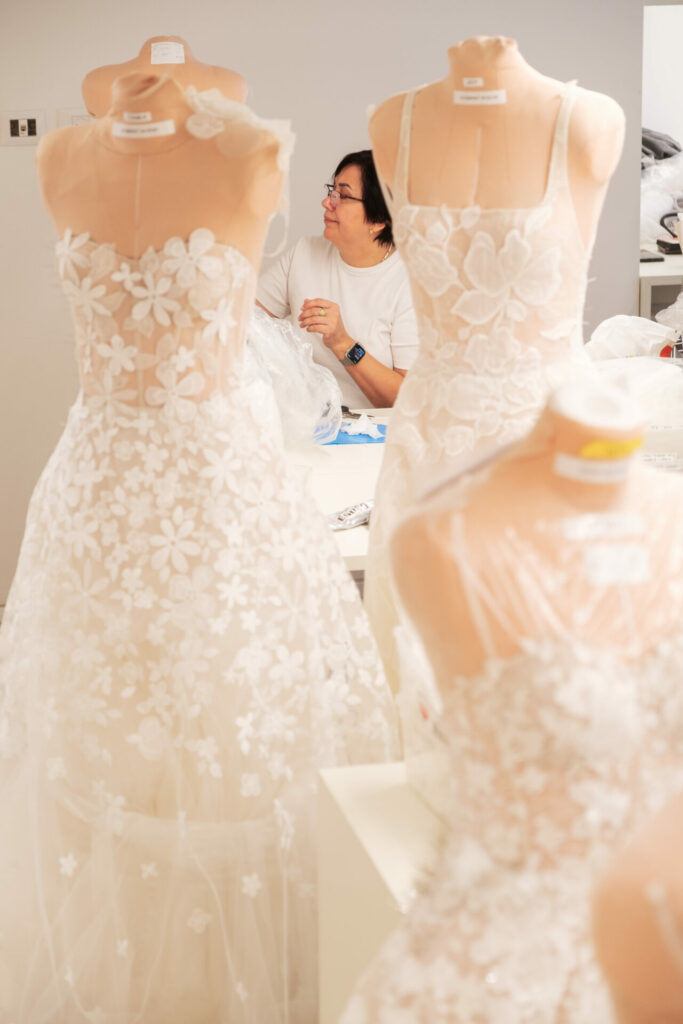 Person at worktable with lace dresses on forms.