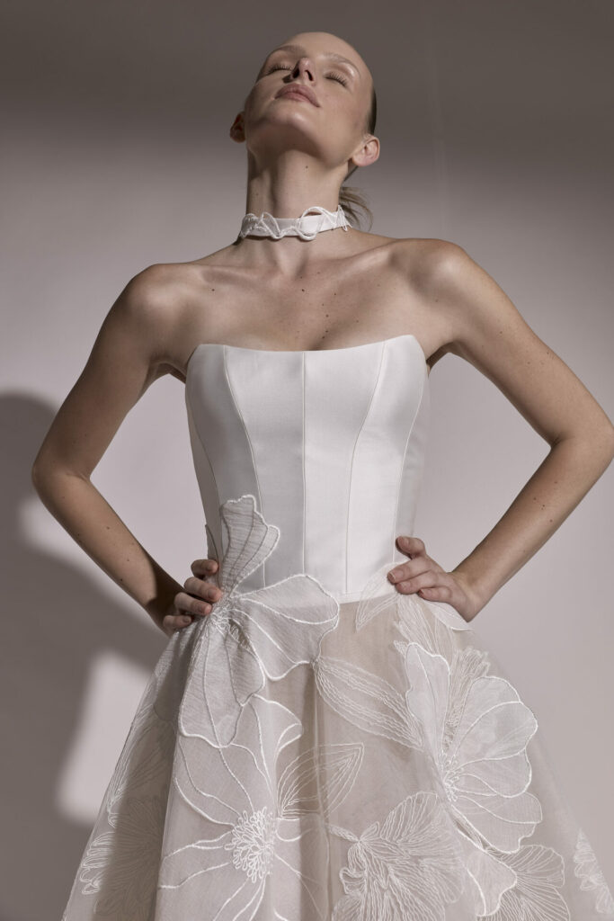 Woman in white floral dress poses, eyes closed.