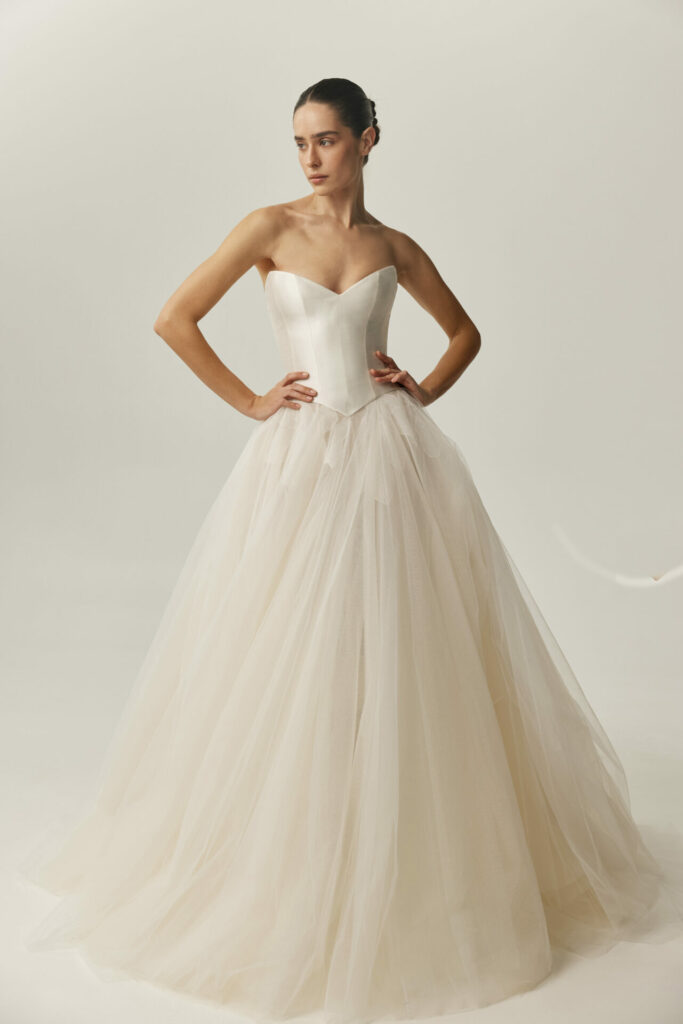 Woman in strapless wedding dress, hands on hips.