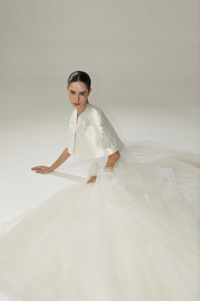 Woman in embroidered white wedding gown sits on floor.