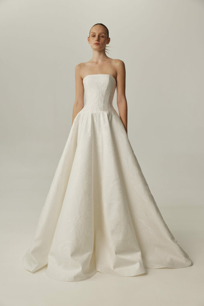 Woman in strapless white gown, hands in pockets.