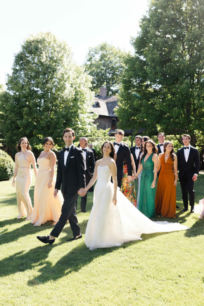 Bride, groom, and wedding party walk on sunny lawn.