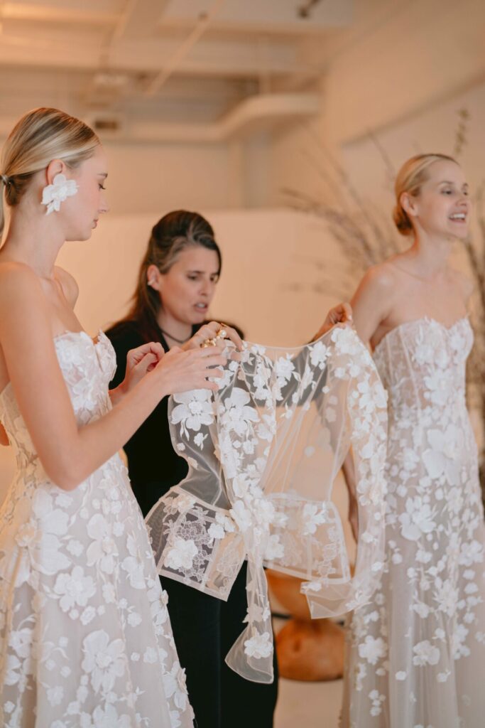Three women in floral white dresses indoors with branches.