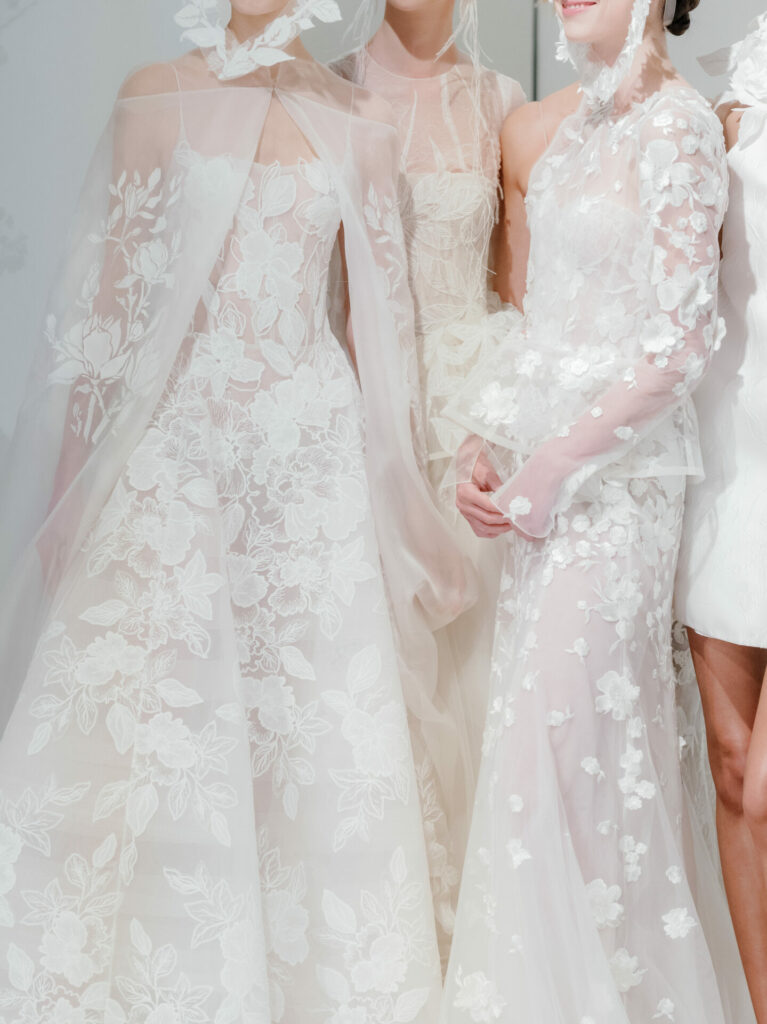 Three women in embroidered sheer white gowns at event.