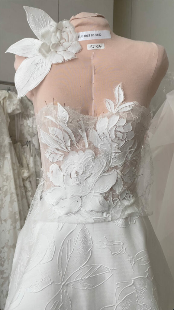 Wedding gown on dress form with lace, flower detail.