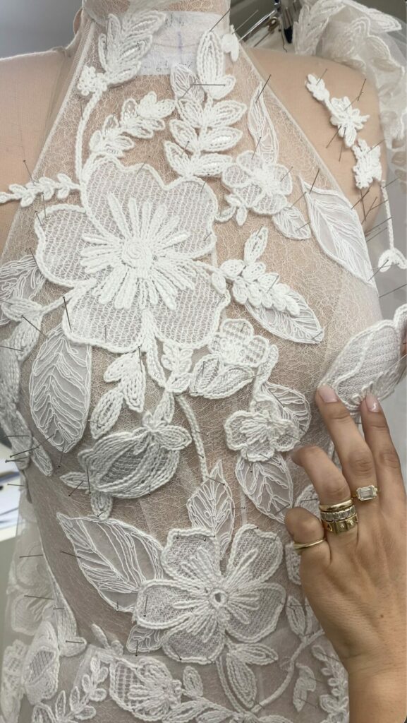 Gold-ringed hand touches white lace on sheer dress.