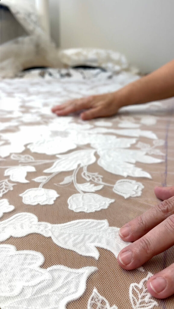 Hands smoothing delicate white floral lace fabric.