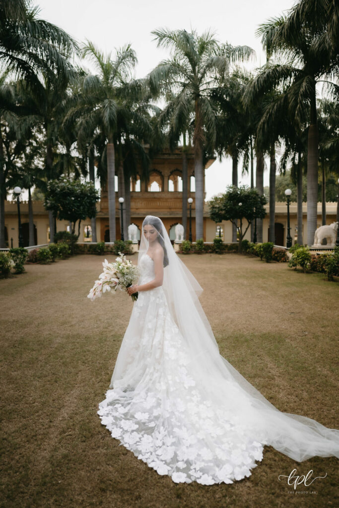 Bride in floral gown and veil poses by grand garden.