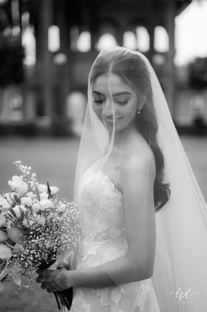 Bride in lace gown, downcast eyes, bouquet outside.