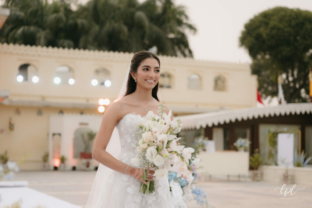 Smiling bride outdoors in white dress with bouquet.