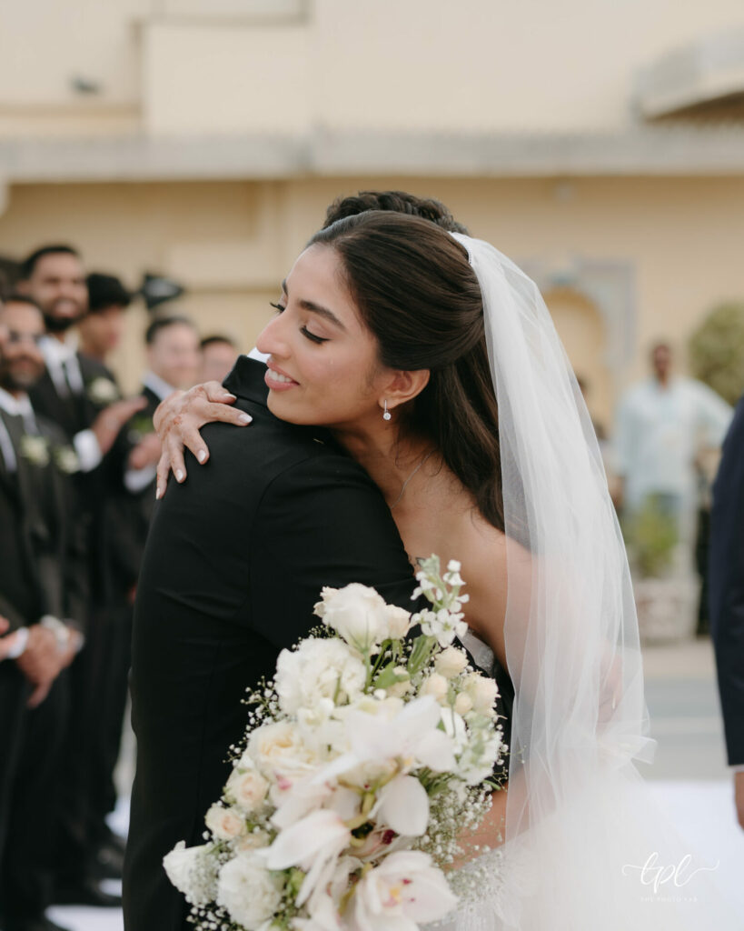 Bride in luxury couture hugs guest at outdoor wedding.