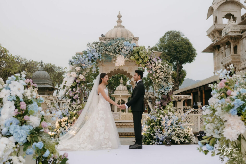 Bride and groom hold hands at ornate outdoor wedding.