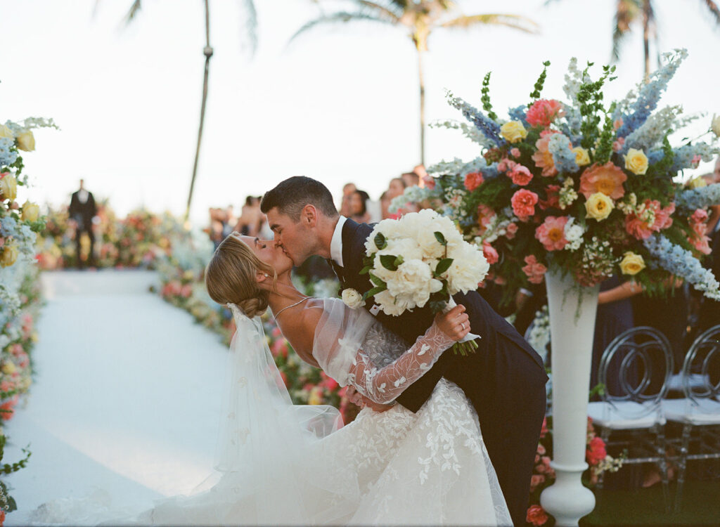 Bride and groom kiss amid elegant outdoor florals.