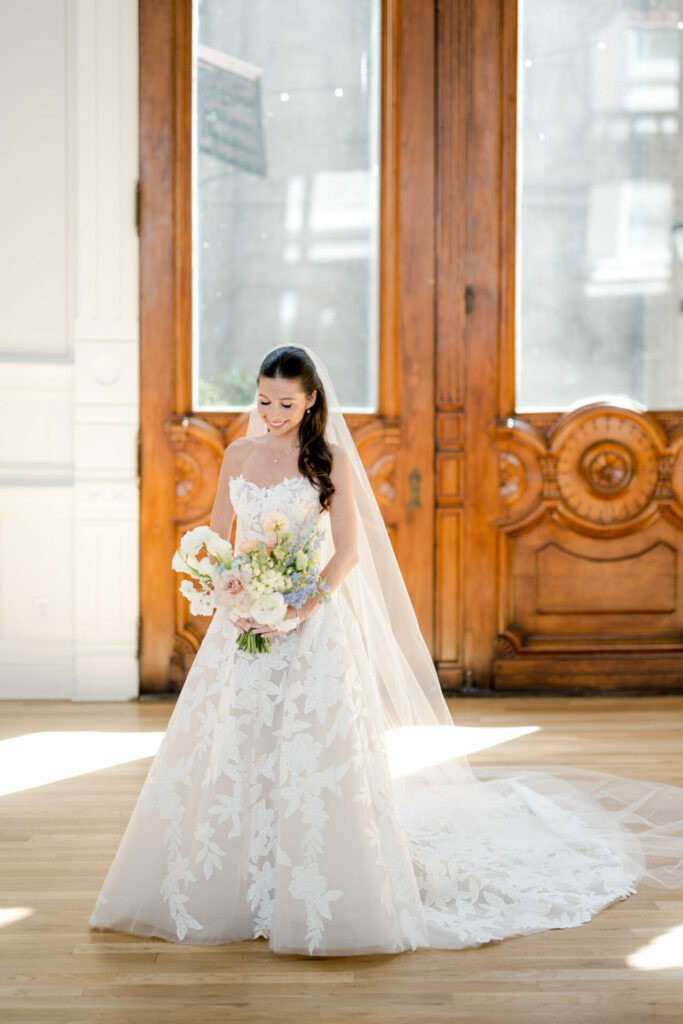 Katya Ruiz smiles in white bridal lace dress, bouquet in hand.
