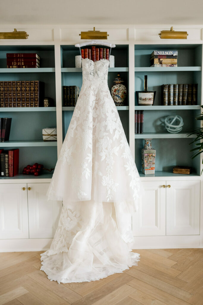 Strapless lace wedding dress hangs on bookshelf.