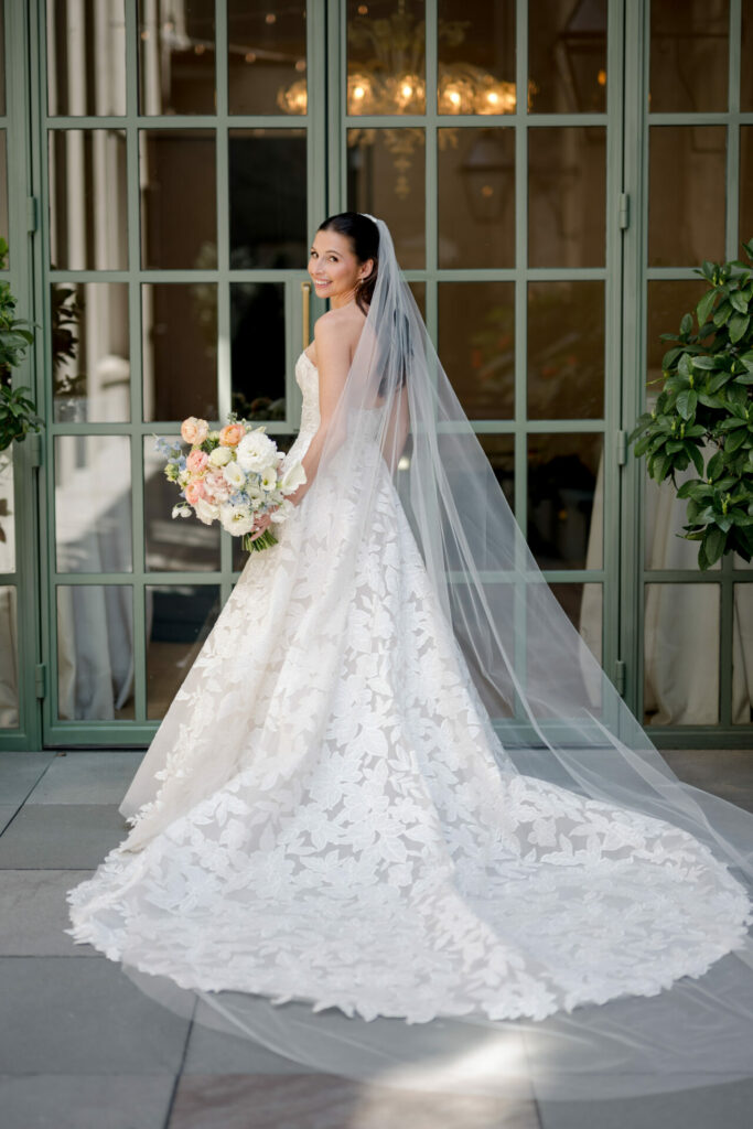 Bride in white lace gown and veil smiles back.