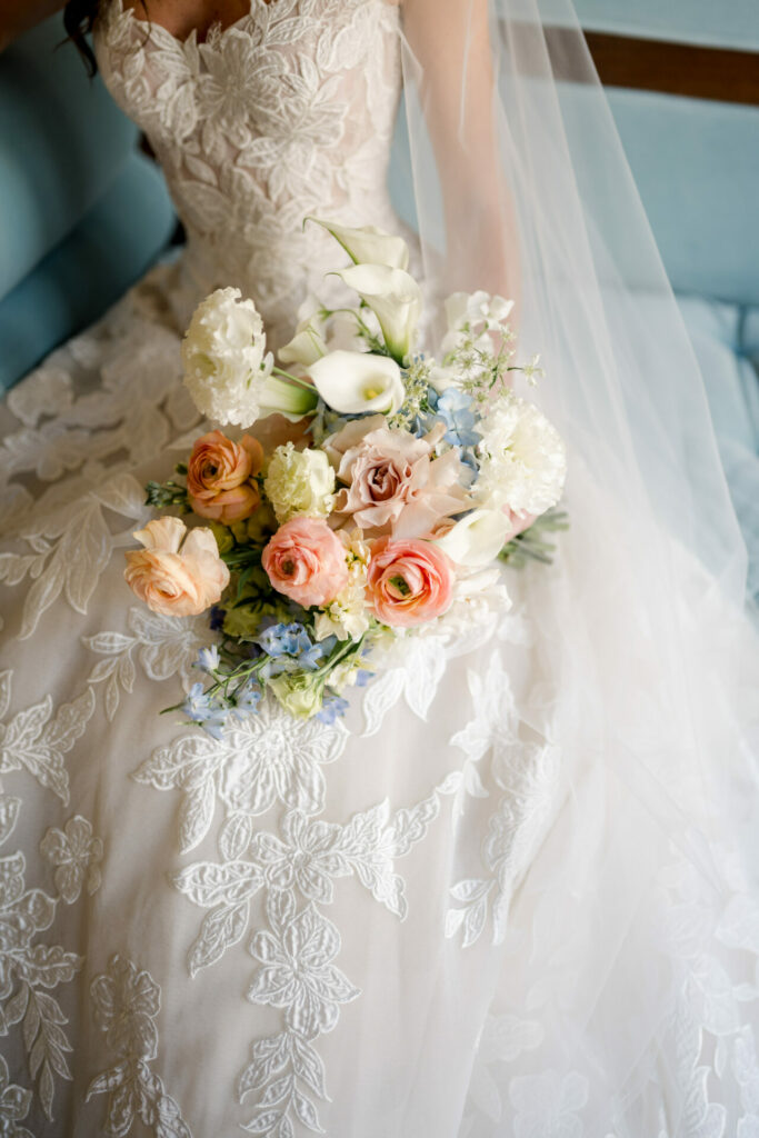 Katya Ruiz in white lace gown, pastel bouquet, seated.