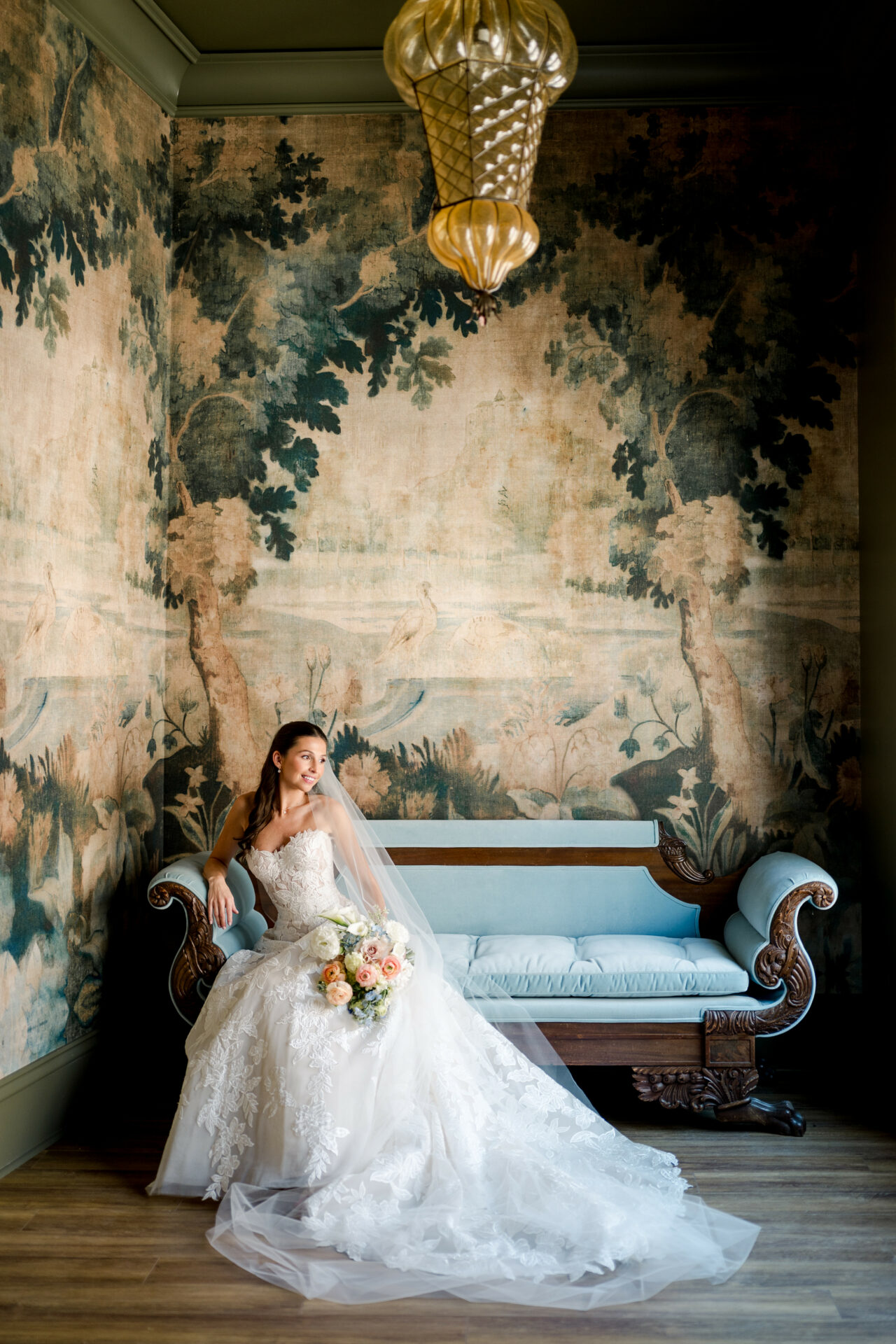Bride in couture on vintage sofa, floral wallpaper.